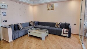 Ein Wohnzimmer mit einem grauen Ecksofa, einem Glastisch, einer Wanduhr und einem gerahmten Bild.