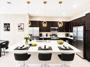 A modern kitchen with dark wood cabinets, stainless steel appliances, and a central island with bar stools. - 24-bedroom luxury villa near Disney (Kissimmee)