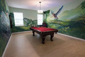 A room with a pool table, green walls with murals, a ceiling light, and a window with blinds. - 24-bedroom luxury villa near Disney (Kissimmee)
