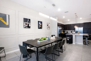 A modern kitchen with dark cabinets, a central island, and a dining area with a dark table and chairs. - 24-bedroom luxury villa near Disney (Kissimmee)