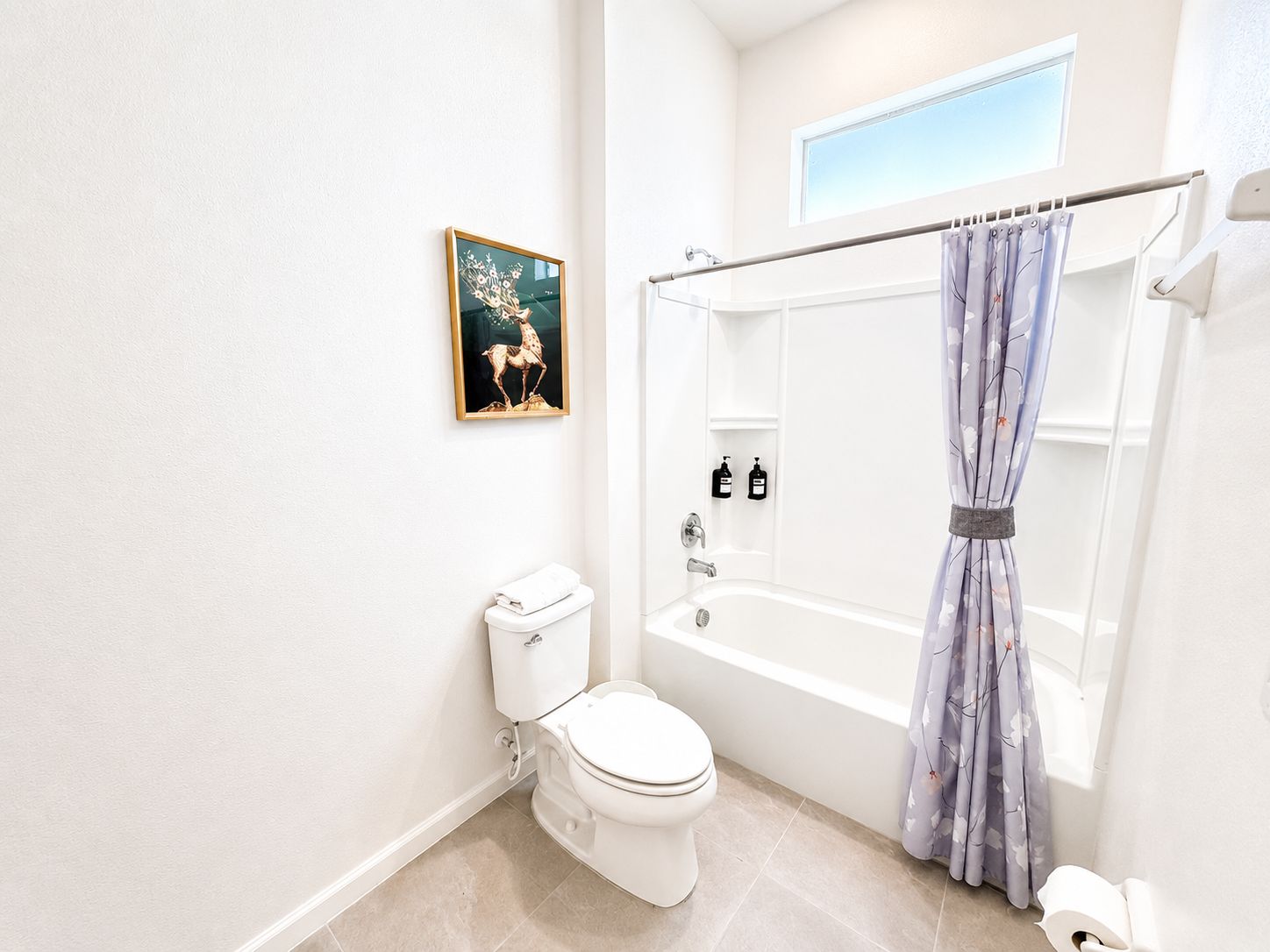 A bathroom with a toilet, bathtub, shower curtain, and a framed picture on the wall.