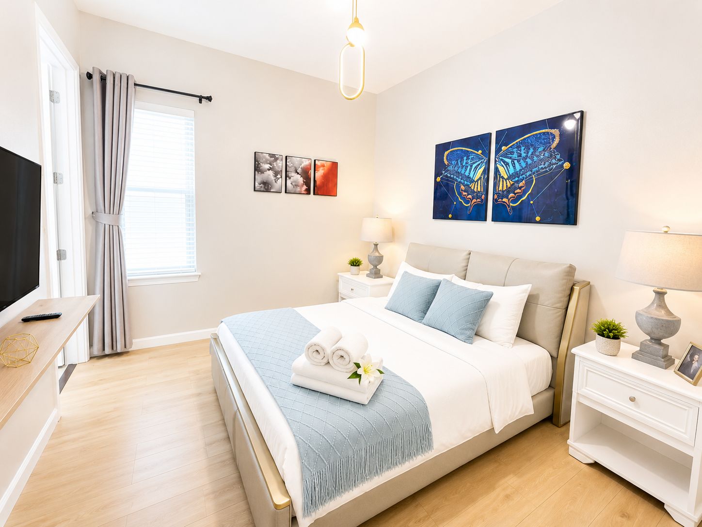 Une chambre à coucher avec un lit, des tables de chevet, une télévision et des œuvres d’art accrochées au mur.