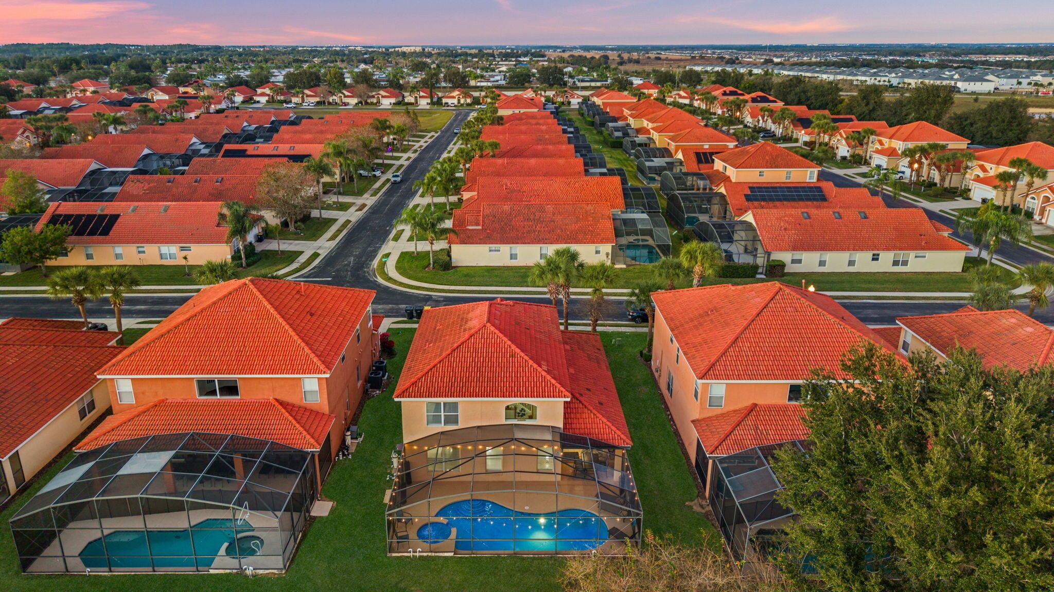 Un quartier résidentiel où les maisons, dotées de toits recouverts de tuiles rouges et de panneaux solaires, sont disposées en rangées de part et d’autre d’une route centrale.