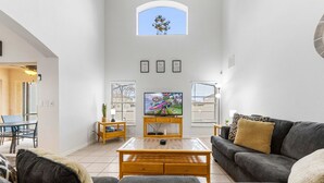Een moderne woonkamer met een flatscreen televisie, een houten salontafel, een grijze bank en een bijzettafeltje met een plant.