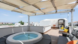 En tagterrasse med jacuzzi, udendørs møbler og udsigt over bybilledet.
