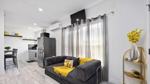 A modern living room with a grey sofa, a yellow throw blanket, and a gold decorative shelf. - Cityscapes Studio Suite #A @ East Downtown (Houston)