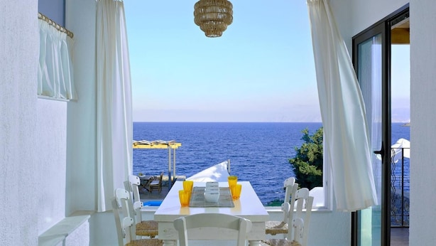 A balcony with a table and chairs, overlooking the sea. - Thalassa Villas (Agios Nikolaos)