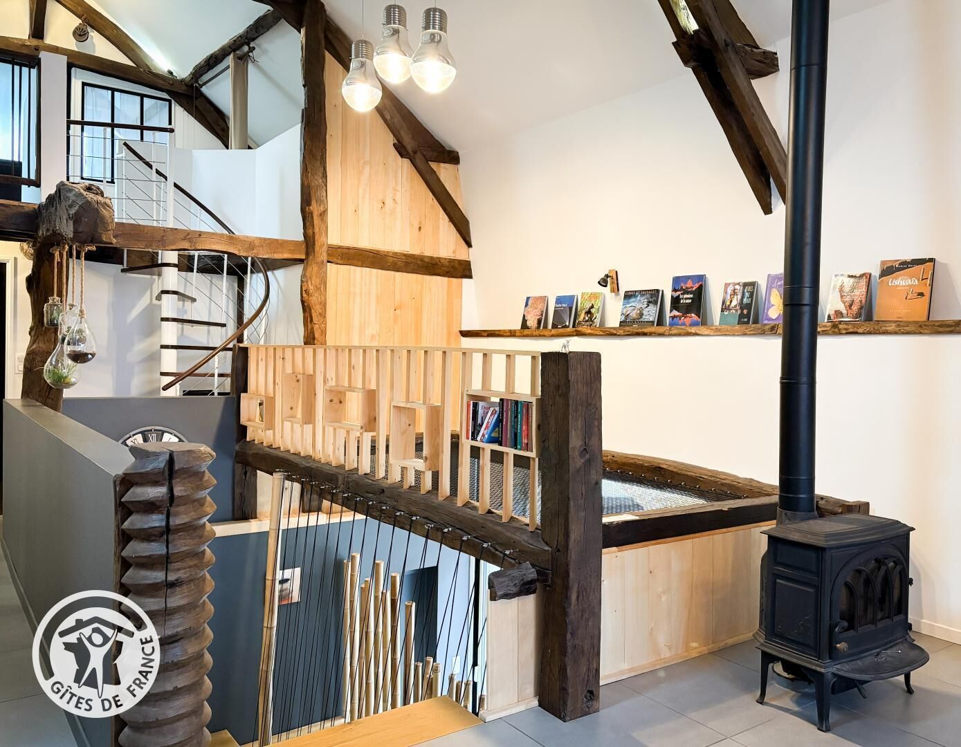 A rustic interior with a wooden staircase, a black wood-burning stove, and a bookshelf with books.
