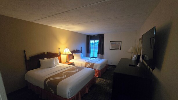 A hotel room with two beds, a desk, a TV, and a window with curtains. - Sunset View Double Queen Room (Houghton Lake)