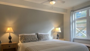 Une chambre à coucher avec un lit, deux lampes de chevet, une fenêtre donnant sur un beau paysage et un ventilateur de plafond.
