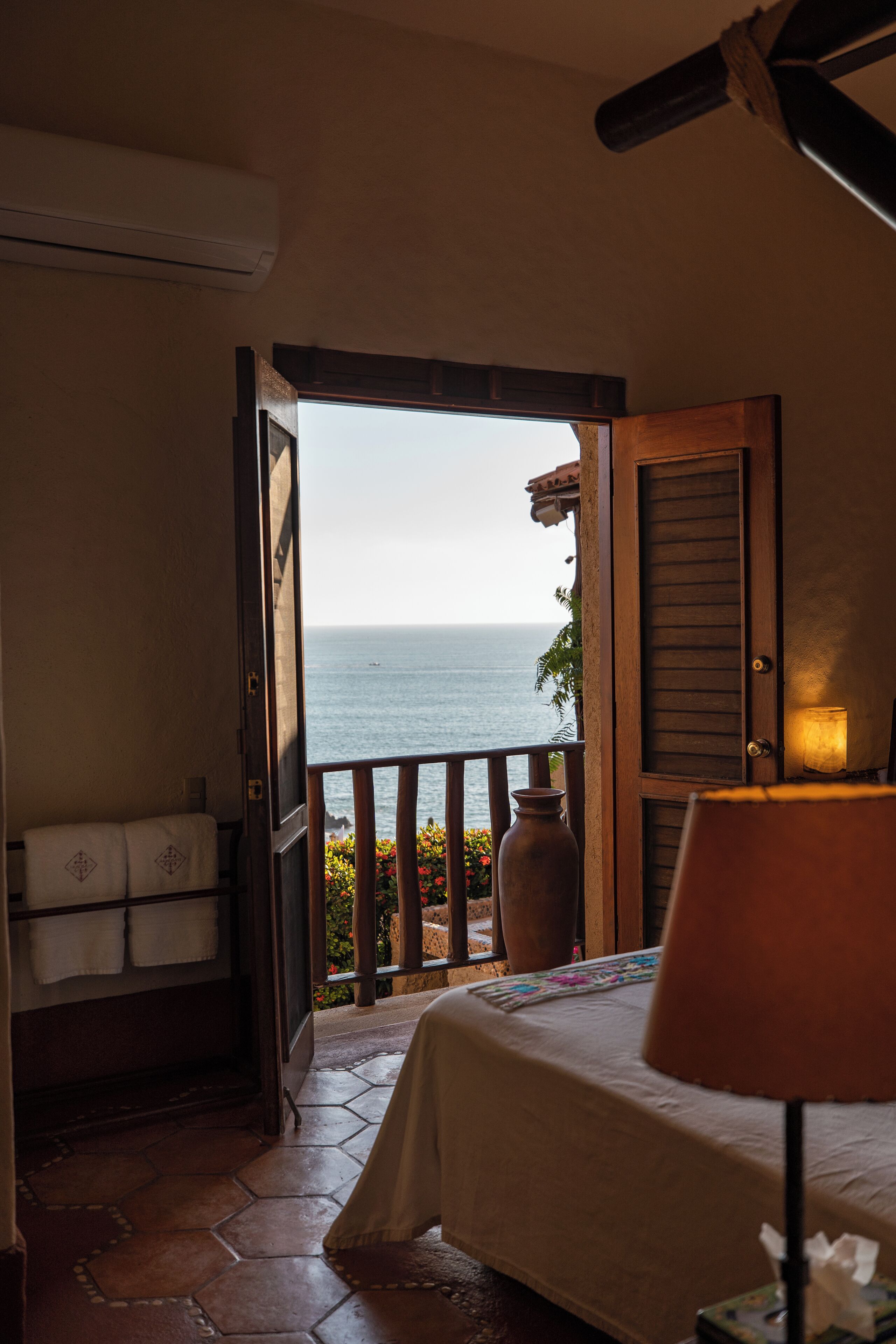 A room with a bed, a lamp, a vase, and a view of the sea.