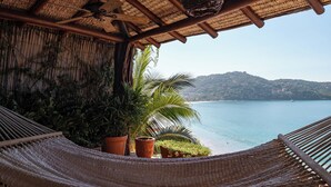 Uma rede sob um telhado de palha, com vista para um corpo de água e colinas.