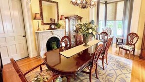 A dining room with a wooden table, chairs, a chandelier, a fireplace, and a large mirror. - Wisteria Suite -The Belvedere Inn (Oswego)