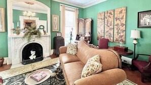 A living room with a fireplace, a sofa, and a chandelier. - Wisteria Suite -The Belvedere Inn (Oswego)