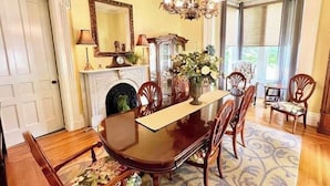 A dining room with a wooden table, chairs, a chandelier, a fireplace, and a large mirror. - Bluebell Room- The Belvedere Inn (Oswego)