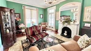A traditional living room with a fireplace, a striped sofa, and a large wooden cabinet. - Magnolia Suite- The Belvedere Inn (Oswego)