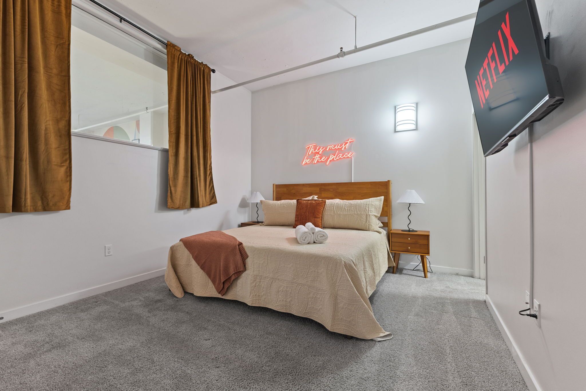 Une chambre à coucher bien rangée, avec un lit, des lampes de chevet, un téléviseur et un panneau lumineux au néon.