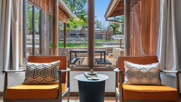 A room with two chairs and a small table, large windows offering a view of an outdoor patio area. - * Stunning FBG Retreat * | Sleeps 10 (Fredericksburg)