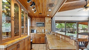 A kitchen with wooden cabinets, a microwave, and a large window overlooking a patio area. - * Stunning FBG Retreat * | Sleeps 10 (Fredericksburg)