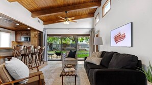 A spacious living area with a dark sofa, wooden chairs, and a coffee table. A ceiling fan and a framed picture are visible. - * Stunning FBG Retreat * | Sleeps 10 (Fredericksburg)