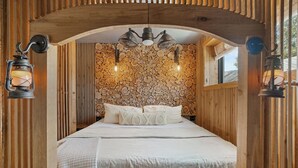 Un dormitorio acogedor con pared de piedra, vigas de madera y dos lámparas de pared tipo farol.