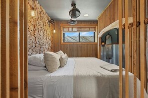 A bedroom with a bed, pillows, a wooden wall, a window, and a ceiling fan. - Unplug, Unwind, and Reconnect at Glowing Embers! (Fredericksburg)