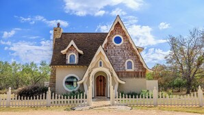 Une maison dotée d’un style architectural particulier, caractérisée par un toit à forte pente, une entrée centrale en arc de cercle et une fenêtre circulaire au deuxième étage.