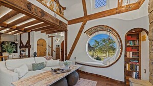Une pièce chaleureuse avec un canapé blanc, une table en bois et une grande fenêtre circulaire donnant sur l’extérieur.