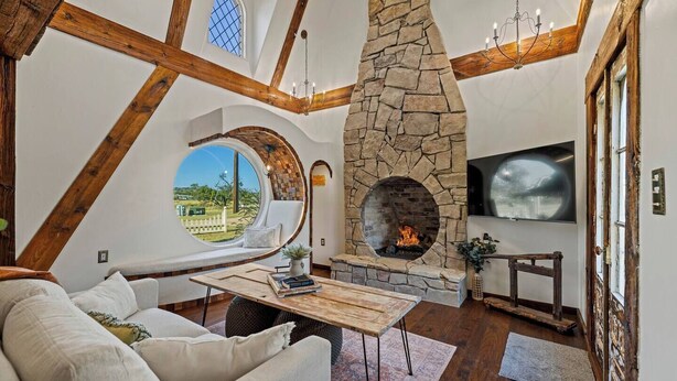 Un salon chaleureux avec une cheminée en pierre, un grand téléviseur et une fenêtre circulaire donnant sur un paysage magnifique.