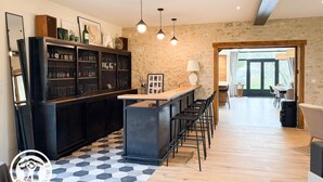 Une cuisine moderne dotée d’un coin bar, avec un sol à motifs hexagonaux, un meuble noir aux portes en verre, un éclairage suspendu et une vue sur la salle à manger.