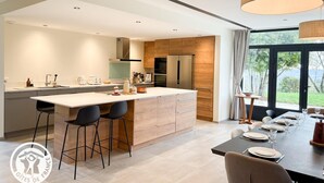 Une cuisine moderne dotée d’un îlot central, de tabourets de bar et d’un coin repas avec une table dressée pour quatre personnes.