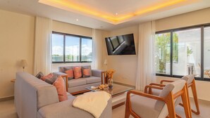 Ein modernes Wohnzimmer mit einer Couch, Sesseln, einem Couchtisch und einem Fernseher.