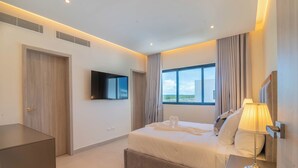 Ein modernes Hotelzimmer mit einem großen Bett, einem Flachbildfernseher, einem Nachttisch mit Lampe und Blick ins Freie durch ein großes Fenster.