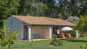 A single-story house with a tiled roof, a covered patio with a table and chairs, and a lawn with two lounge chairs. - Lefkes Apartments (Corfu)
