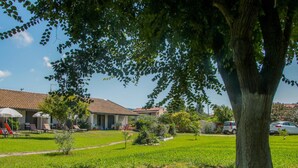 A hotel with a tiled roof, outdoor seating area with umbrellas, and a well-maintained lawn. - Lefkes Apartments (Corfu)