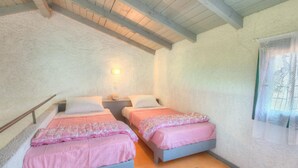 A bedroom with two beds, a nightstand, a wall-mounted light, and a window with a white curtain. - Lefkes Apartments (Corfu)
