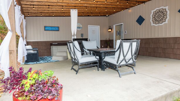 En udendørs terrasse med et træbeklædt pergolaoverhang, et bord med stole, og et skilt, der står "velkommen til vores skønne sted".