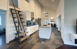 Una cuina moderna amb una illa central, electrodomèstics integrats i una escala de fusta.