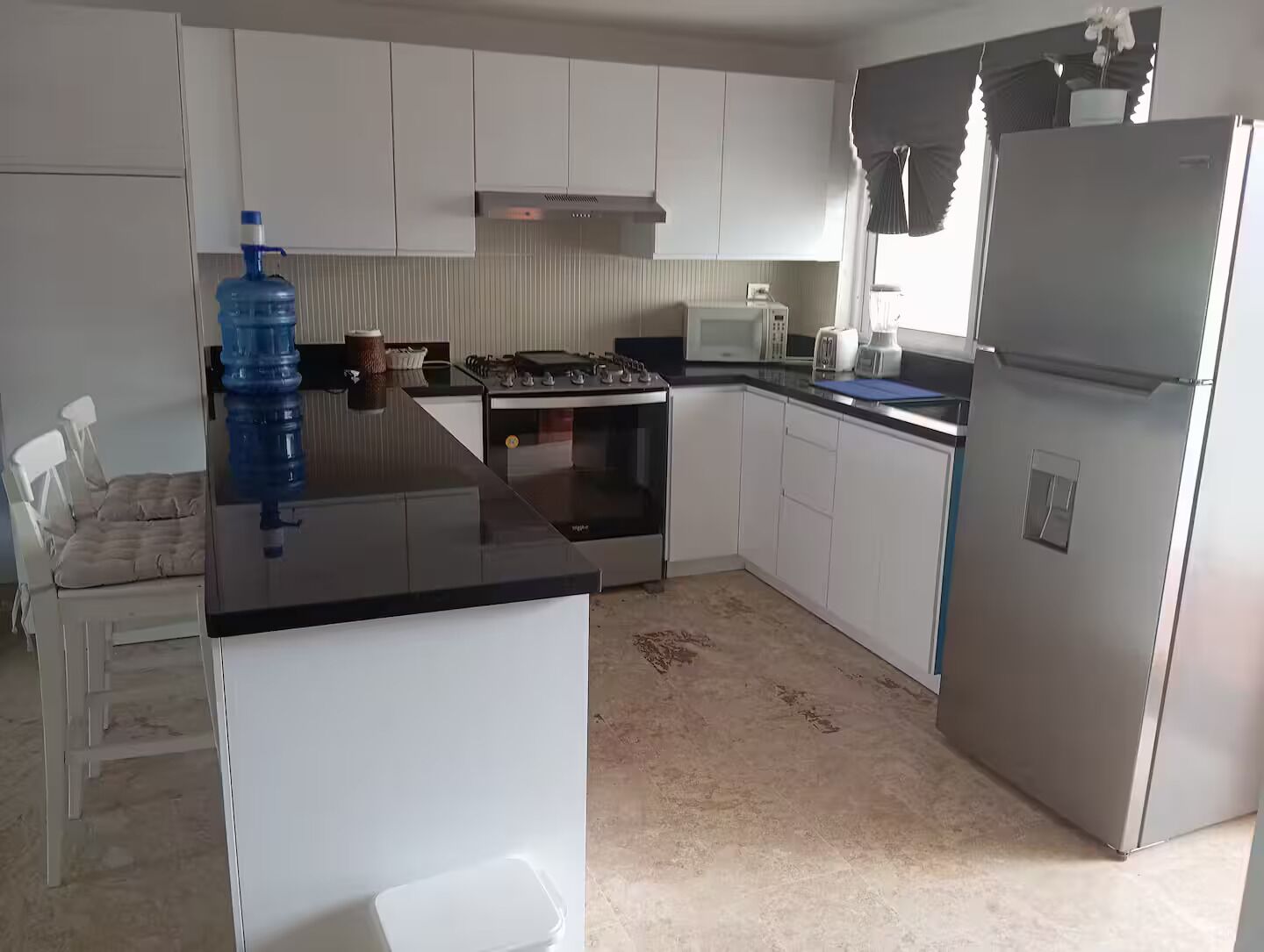 A modern kitchen with white cabinets, a stainless steel refrigerator, a microwave, a stove, and a water dispenser.