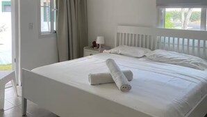 A bedroom with a bed, a ceiling fan, a nightstand with a lamp, and a window with blinds. - Beach Apartment in Stanza Mare Punta Cana (Punta Cana)