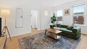 A modern living room with a green sofa, wooden coffee table, and a large rug. - Stunning City Views · Midtown Heart of Detroit · Clean · Free Parking (Detroit)