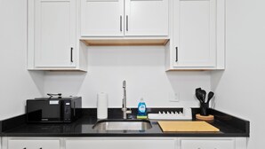 A kitchen with white cabinets, a black countertop, a microwave, a sink, and a cutting board. - Stunning City Views · Midtown Heart of Detroit · Clean · Free Parking (Detroit)
