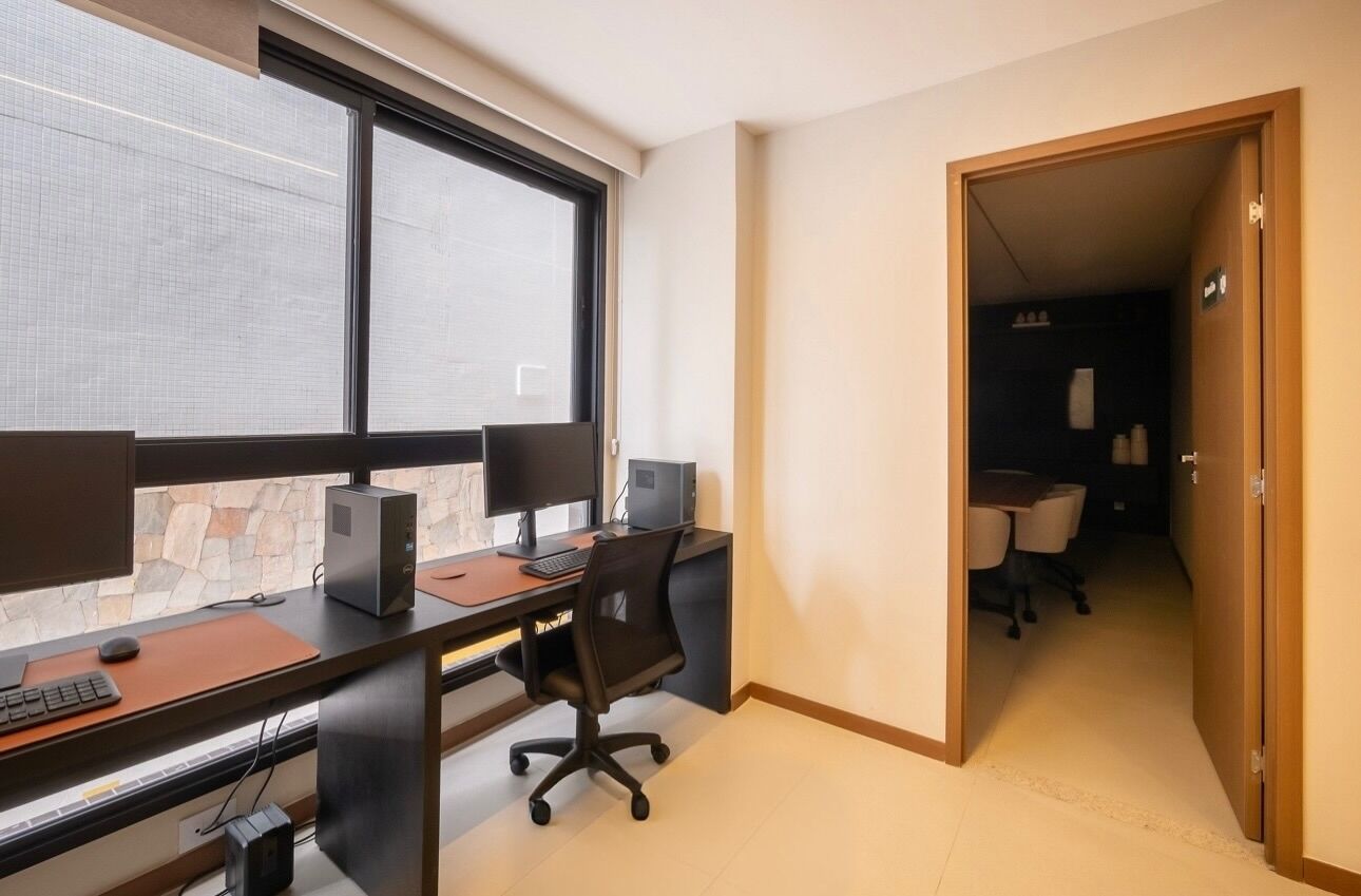 Un espace de bureau moderne doté d’une grande fenêtre, d’un bureau avec deux écrans, d’une chaise et d’un ordinateur.