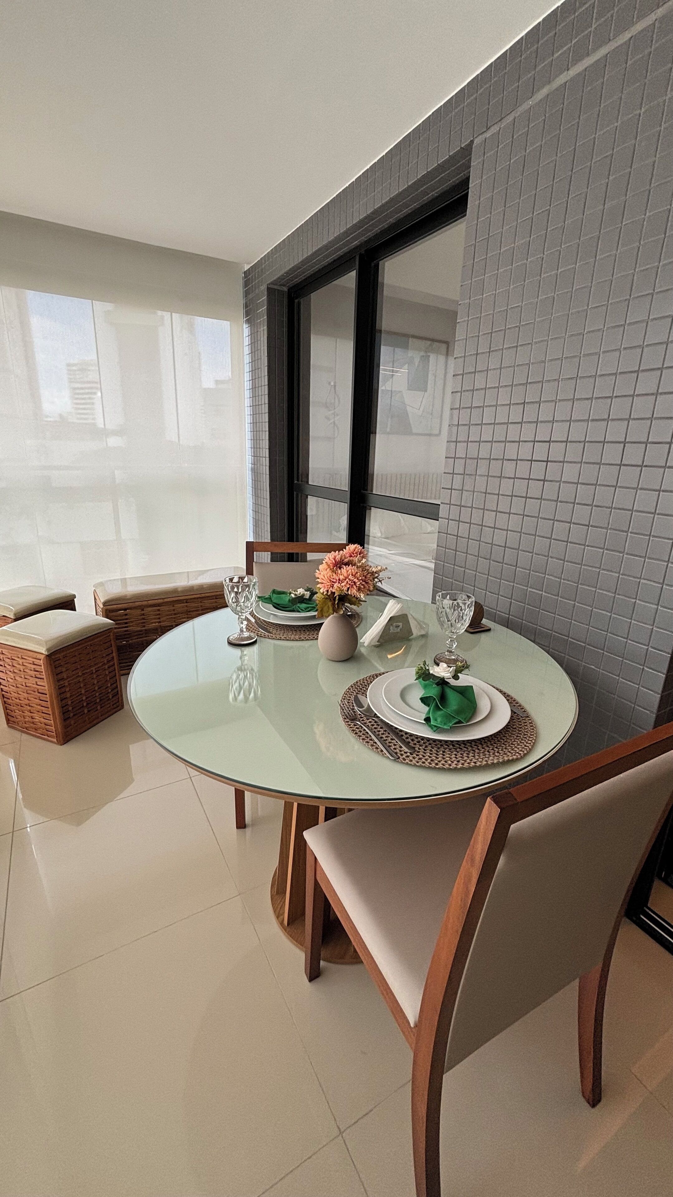 A modern dining area with a glass table, wicker chairs, and a view of the city through large windows.