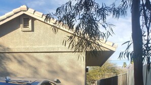 Un coche deportivo plateado estacionado en una entrada con superficie de grava, un camino de hormigón y una casa con pared exterior texturizada.