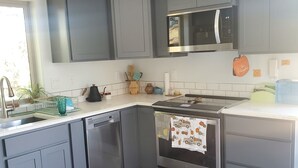 Una cocina moderna con gabinetes grises, un microondas de acero inoxidable, un lavavajillas y un horno con un paño decorativo.
