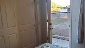 Un dormitorio con una cama, una puerta cerrada y un ventanal corredero que da a un espacio exterior.