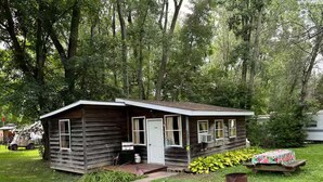 A small wooden cabin with a porch, surrounded by lush greenery. - Charming 2-bedroom cabin with AC in West Chazy (West Chazy)