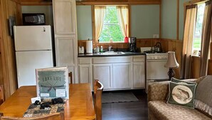 A cabin interior with a wooden dining table, chairs, a sofa, and a kitchen area including a refrigerator, microwave, and stove. - Charming 2-bedroom cabin with AC in West Chazy (West Chazy)
