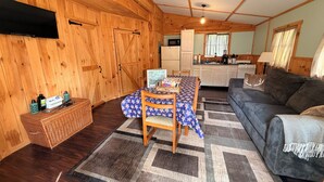 A wooden interior with a dining table, sofa, kitchen area, and a television mounted on the wall. - Charming 2-bedroom cabin with AC in West Chazy (West Chazy)